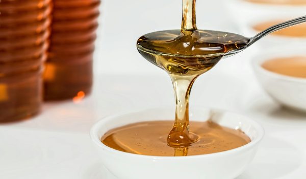 Delicious honey pouring slowly from a spoon into a white bowl, highlighting its golden hue and viscosity.